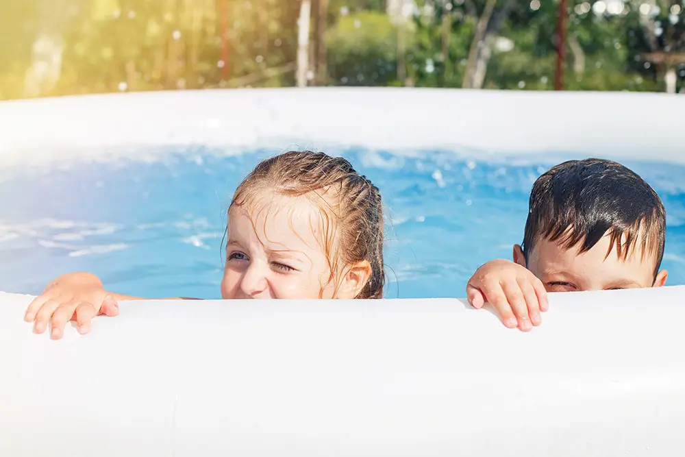 Två barn tittar över kanten på en pool och leker i vattnet en solig dag.